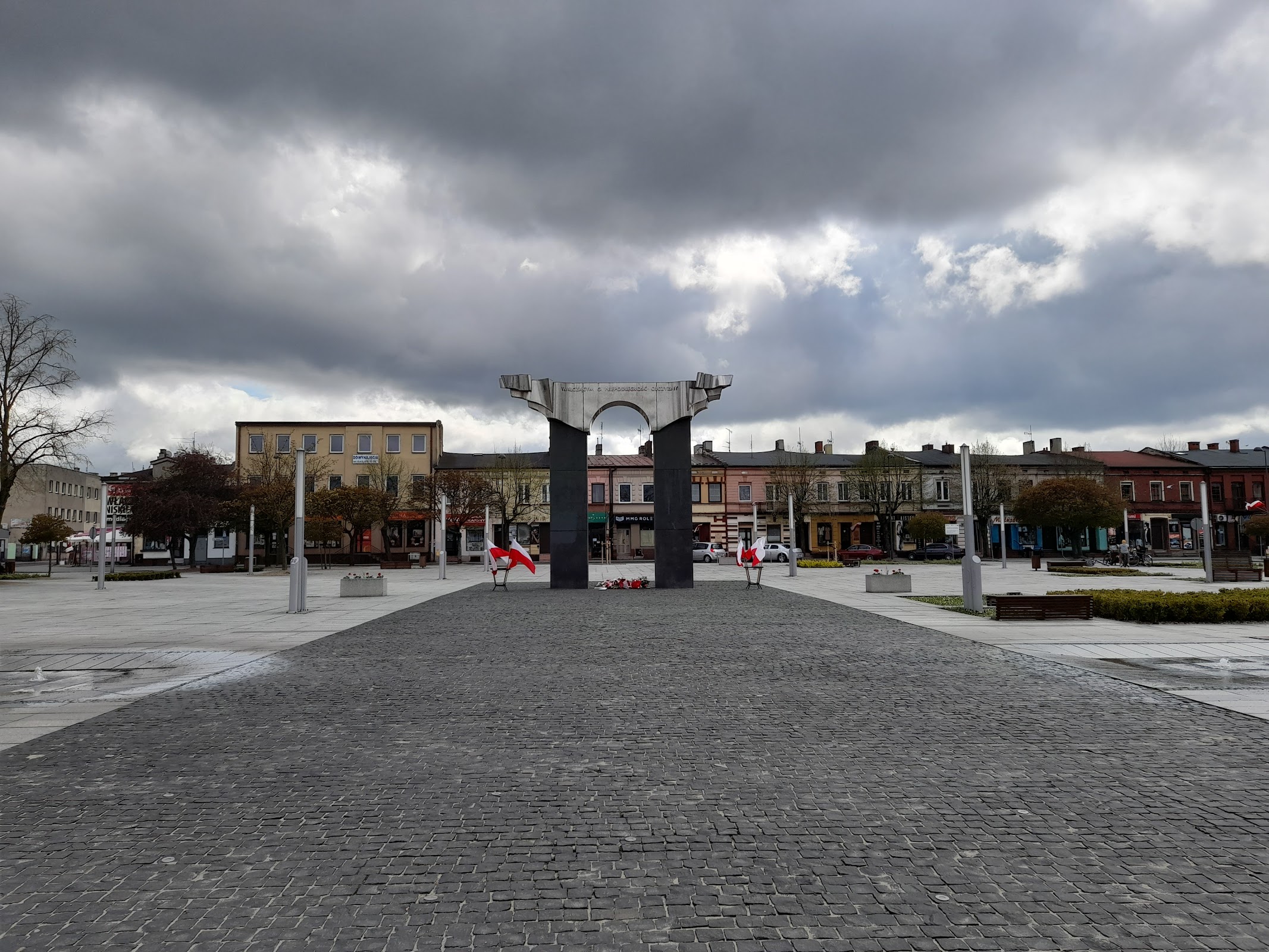 Plac 11 Listopada w Łasku z pomnikiem, lokalna architektura. Lokal stoi dwa kroki od Rynku.