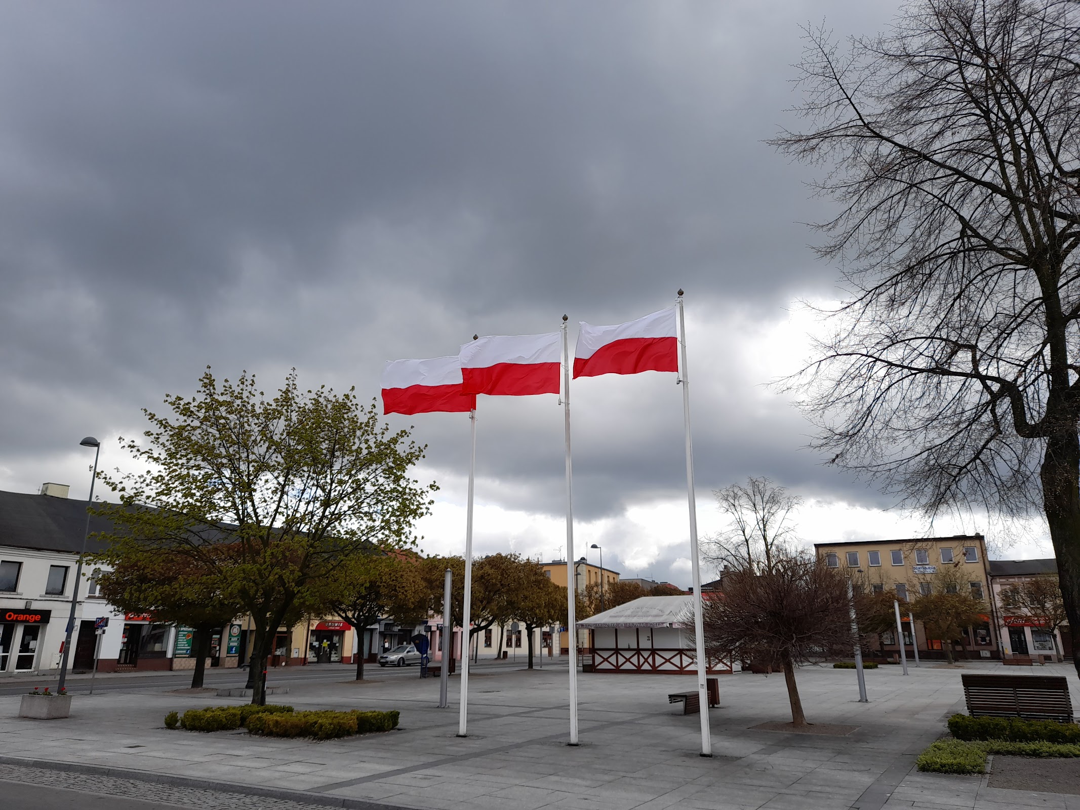 Rynek w Łasku, Plac 11 Listopada, biało-czerwone flagi i pomnik. Dwie minuty piechotą od lokalu.